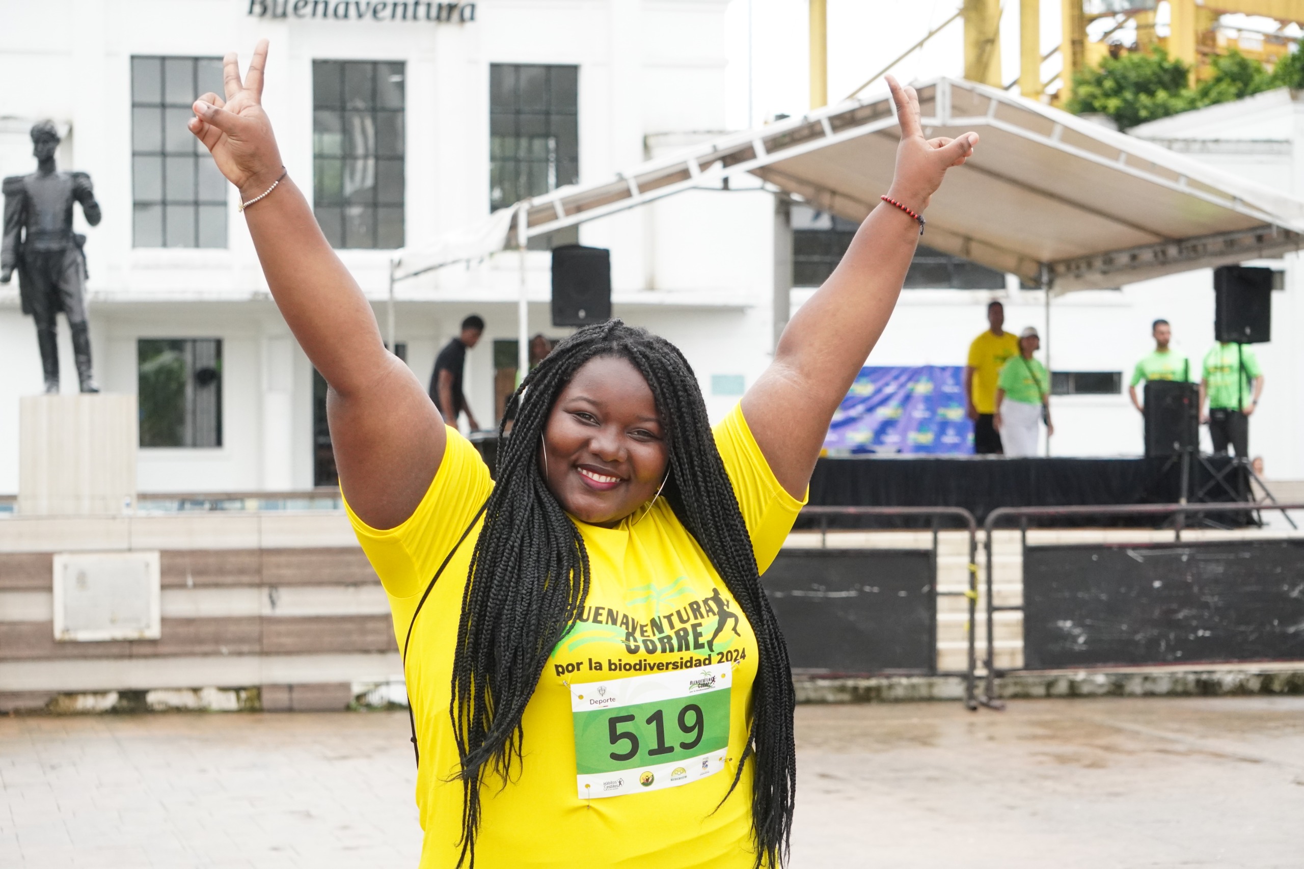 En la imagen se observa una mujer afrocolombiana con las manos arriba y su la camiseta de la carrera Buenaventura Corre 2024